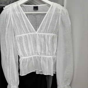 Vit blus med v-ringning från Gina Tricot - Säljer en luftig vit blus från Gina Tricot med v-ringning och långa puffärmar. Blusen har en lätt rynkad struktur och markerad midja för en feminin siluett. Perfekt till vår och sommar! NY!