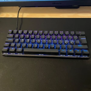 Apex 9 mini - Säljer ett kompakt svart mekaniskt tangentbord från SteelSeries med RGB-belysning. Tangentbordet har en minimalistisk design utan numerisk del och ansluts med kabel. Perfekt för gaming eller skrivbordet.