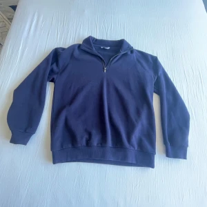 Mörkblå sweatshirt med halv dragkedja - En stilren mörkblå sweatshirt med halv dragkedja i halsen. Tröjan har långa ärmar, ribbade muddar och en klassisk passform. Perfekt för en avslappnad och sportig look.