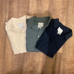Tre kortärmade skjortor i tre färger Mörkblå, grön & beige - Säljer tre stilrena kortärmade skjortor från 157 i färgerna marinblå, grågrön och beige. Skjortorna har klassisk krage, bröstficka och knäppning framtill. Perfekta för en avslappnad men snygg look. Storlek Medium på alla tre. Snabb Leverans!