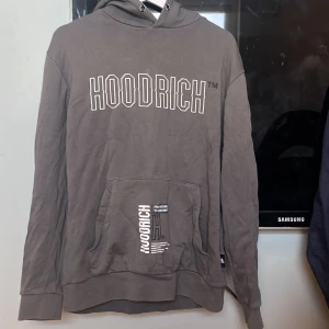 Grå hoodie från Hoodrich - Säljer en grå hoodie från Hoodrich med stor vit logga framtill och vertikal logga på ryggen. Tröjan har huva och en stor magficka. Perfekt för en avslappnad stil. Den är väldigt skön och nytt skick, säljs då jag inte använder den längre. Den är väldigt skön och går och matcha med det mesta! Pris diskuterbart