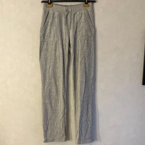 Grå mjukisbyxor från Juicy Couture - Grå mjukisbyxor från Juicy Couture med dragsko i midjan och fickor både fram och bak. Byxorna har raka ben och är tillverkade i mjukt bomullsmaterial. Perfekta för en avslappnad stil.