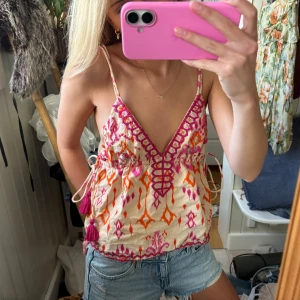 Mönstrad linnetopp - Säljer en superfin linnetopp med broderade mönster i orange och rosa. Toppen har smala axelband, djup v-ringning och knyt i sidorna. Verkligen så fint och coolt mönster och passar så bra till sommaren🌸☀️🩷