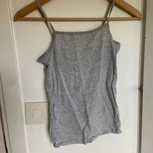 Grå linnetopp från H&M - Säljer en enkel och stilren grå linnetopp från H&M Basic i ekologisk bomull i barnstorlek. Toppen har smala axelband och rak halsringning, perfekt för varma dagar eller som lager under andra plagg.