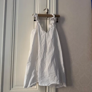 Vit somrig klänning med volangaxelband - Säljer en söt vit klänning med volangdetaljer på axelbanden. Klänningen har en v-ringad hals och är ärmlös, perfekt för varma dagar. Lätt och luftig modell som ger en avslappnad känsla. Den är uppsydd sen innan och kan vara lite stor i axelbanden💗