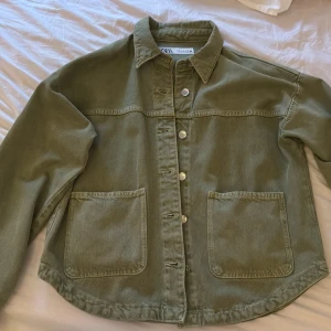 Olivgrön overshirt från ZARA - Säljer en olivgrön overshirt från ZARA i storlek XS. Jackan har två stora fickor framtill, knappar längs hela framsidan och klassisk krage. Perfekt att slänga över en t-shirt för en avslappnad look.