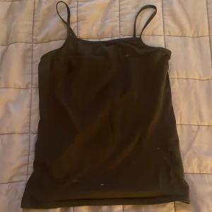 Svart linnetopp från H&M - En enkel svart linnetopp från H&M Basic i ekologisk bomull. Toppen har smala axelband och rak passform, perfekt för varma dagar eller som lager under andra plagg.