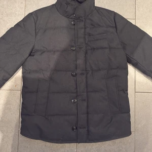 Svart jacka med knappar - Riktigt snygg svart John Henric jacka med hög krage och knäppning framtill. Jackan har två stora fickor på sidorna och en bröstficka. Fodrad insida med dragkedja. Perfekt för våren och kyligare sommardagar!