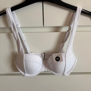 Vit bikiniöverdel från Bik Bok - Säljer en stilren vit bikiniöverdel från Bik Bok i storlek XS. Modellen har breda axelband, bygel och knäppning bak. Perfekt för dig som vill ha en enkel och klassisk look på stranden.