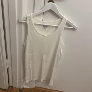 Vit linnetopp från A.O.CMS - Säljer en enkel och stilren vit linnetopp från A.O.CMS i storlek M. Toppen är ärmlös med rund halsringning och tillverkad i ett mjukt material som passar perfekt till sommaren.