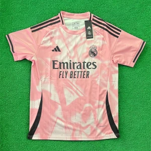 Rosa Real Madrid fotbollströja från Adidas - Säljer en rosa Real Madrid fotbollströja från Adidas med svarta detaljer och klubbmärke på bröstet. Tröjan har korta ärmar, svart Adidas-logga och sponsortryck på framsidan. Perfekt för fotbollsträning eller som supporterplagg.
