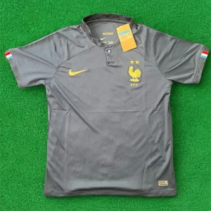 Frankrike fotbollströja Nike grå/guld - Säljer en grå fotbollströja från Nike med Frankrikes landslagsmärke och två stjärnor i guld på bröstet. Tröjan har korta ärmar och gul Nike-logga. Små franska flaggor på ärmsluten. Perfekt för fotbollsfans!