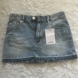 Blå jeanskjol från Pull&Bear - Säljer en klassisk blå jeanskjol från Pull&Bear i kort modell. Kjolen har råa kanter nertill, femficksdesign och en liten sliten detalj framtill. Prislapp kvar då den inte passade mig. 