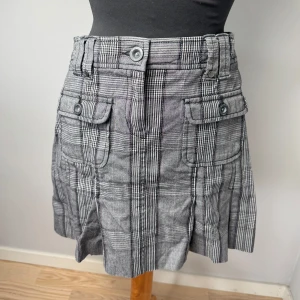 Grå rutig kjol från Esprit - Grå kortkjol från Esprit med rutigt mönster och stora fickor framtill med knappar. Perfekt för dig som gillar en retro och cool stil. Storlek M och är aldrig använd🩷