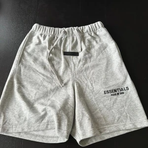 Grå shorts från Essentials Fear of God - Snygga grå shorts från Essentials Fear of God med elastisk midja och snörning. Mjukt material och logga tryckt på benet. Perfekta för en avslappnad stil.