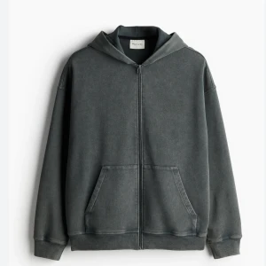 Mörkgrå hoodie med dragkedja - Säljer en mörkgrå hoodie från Pull&Bear med dragkedja framtill och känguruficka. Tröjan har luva och långa ärmar, perfekt för en avslappnad stil. Passformen är normal och materialet känns mjukt och bekvämt.