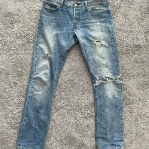 Levis 501 slitna blå jeans - Säljer ett par klassiska Levis 501 jeans i ljusblå denim med slitningar och hål på benen för en cool, avslappnad look. Rak passform och normal midja. Strl W30 L31