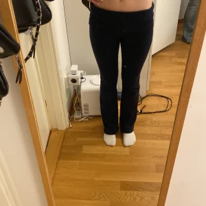 Mörkblå stickade byxor från Gina Tricot - Mörkblå stickade byxor från Gina Tricot med bred ribbad midja och utsvängda ben. Byxorna har en mjuk och bekväm känsla, perfekta för en avslappnad stil. Passformen är normal och materialet är stickat så därför har den blivit lite nopprig i tvätten.