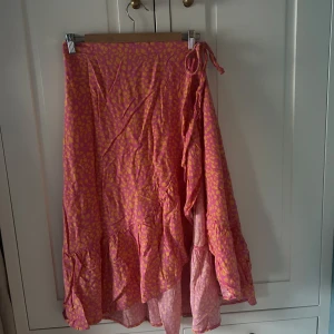 Rosa och orange omlottkjol från Pernilla Wahlgren - Säljer en färgglad omlottkjol från Pernilla Wahlgren i rosa och orange med volangkant. Kjolen har knytband i midjan och ett leopardaktigt mönster. Perfekt för dig som gillar färg och vill ha något unikt! 🪸⭐️