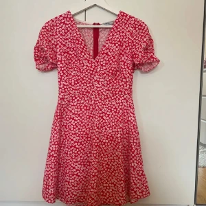 Röd blommig klänning - Supersöt röd kortklänning från Chiquelle med vitt blommönster. Klänningen har v-ringning, korta puffärmar och markerad midja. Väldigt bra skick! 