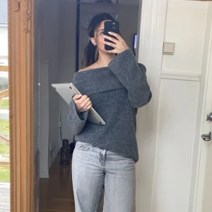 Grå offshoulder stickad tröja - Mysig grå stickad tröja med bred offshoulder-krage. Tröjan har lång ärm och en avslappnad passform.