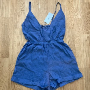 Blå omlott jumpsuit från Zaful - Säljer en blå jumpsuit från Zaful med omlott framtill och smala axelband. Helt nytt, för liten för mig.