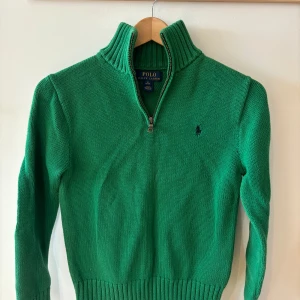 Grön stickad tröja med dragkedja från Polo Ralph Lauren - Säljer en grön stickad tröja från Polo Ralph Lauren med halv dragkedja och hög krage. Tröjan är för 10-12 åringar eller storlek M barn