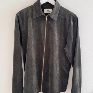 Grön manchester overshirt från Cizsere - Säljer en stilren grön overshirt i manchester från Cizsere. Overshirten har lång ärm, klassisk krage och dragkedja framtill. Perfekt för lager-på-lager och ger en avslappnad men snygg look.