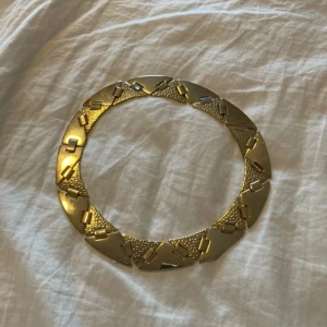 Guldfärgat statement-halsband - Säljer ett chunky halsband i guldfärgad metall med geometriskt mönster. Halsbandet har breda länkar och sitter nära halsen för en cool och modern look. Perfekt för att lyfta en enkel outfit.