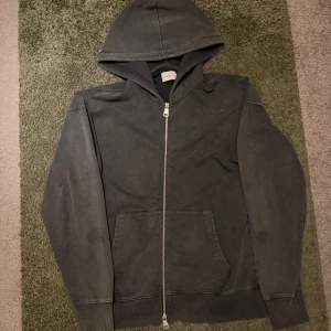 Mörkgrå hoodie med dragkedja - Säljer en mörkgrå hooie med dragkedja framtill och huva. Tröjan har två stora fickor och ribbade muddar vid ärmslut och nederkant. Perfekt för en avslappnad stil.