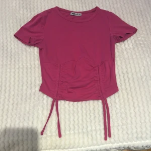 Rosa topp med knyt från new yorker  - Säljer en rosa topp i storlek XS. Toppen har korta ärmar och snygga knytband framtill som ger en trendig look. Perfekt för dig som vill ha en enkel men ändå detaljrik topp till garderoben.