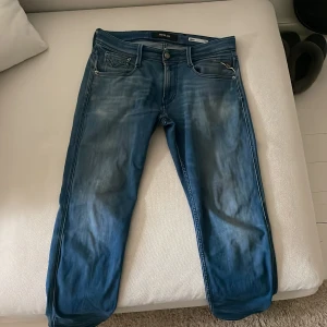 Replay Anbass - Säljer ett par blå Replay Anbass jeans i slim fit med klassisk femficksdesign och snygga slitningar. Jeansen har normal midja och raka ben, tillverkade i mjukt denimtyg. Passar perfekt till dig som gillar en smalare passform.