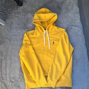 Gul hoodie från Polo Ralph Lauren - Snygg gul hoodie från Polo Ralph Lauren med klassisk broderad logga på bröstet. Tröjan har huva med vita snören och en stor magficka framtill. Perfekt för dig som gillar en färgglad och stilren look. Säljer den på vinted bara clothes_clothesssss För endast 349kr