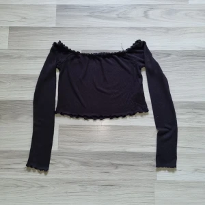 Svart offshoulder topp från BikBok - Säljer en svart offshoulder topp från BikBok med långa ärmar. Toppen har vågiga kanter vid halsringning, ärmslut och nederkant. Perfekt för dig som gillar en trendig och stilren look.