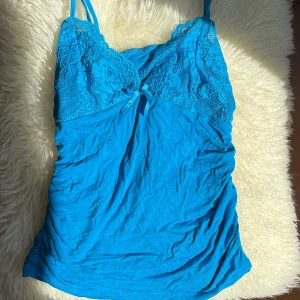 Blå spetslinnetopp med rosett - Säljer en blå linnetopp med spetsdetaljer upptill och en liten rosett framtill. Toppen har smala axelband och är figurnära. Perfekt för sommaren❤️❤️ Står ingen storlek men skulle säga att den passar xs-m💕