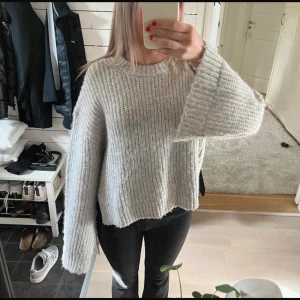 Grå stickad tröja  - Ljusgrå stickad tröja med slits vid båda sidor av tröjan och längst ner vid båda ärmarna. Använd fåtal gånger så tröjan är bra kvalitet. Tröjan är ganska kort och boxig.