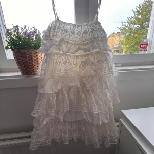 Vit volangklänning från Zara - Supersöt vit klänning från Zara med tunna axelband och flera lager volanger. Klänningen har spetsdetaljer och ett luftigt uttryck. Perfekt för varma dagar eller speciella tillfällen. Säljes då den inte längre kommer till användning. Använd några fåtal gånger och är i nyskick🥰