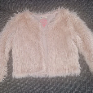 Ljusrosa pälsjacka från H&M - Supermjuk och fluffig ljusrosa pälsjacka från H&M. Jackan har lång ärm, öppen framtill och är helfodrad med glansigt tyg. Perfekt för dig som vill sticka ut med en trendig och cozy look.