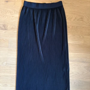 Plisserad marinblå långkjol från  - Säljer en svart plisserad långkjol i storlek XS. Kjolen har elastisk midja och ett snyggt fall med smala veck. Perfekt för dig som gillar stilrena och tidlösa plagg med en modern twist.
