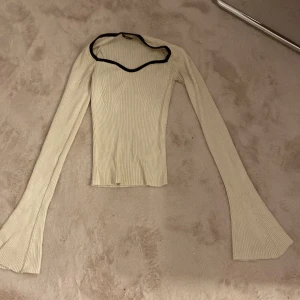 Ribbad vit långärmad topp Gina Tricot - Supersnygg ribbad vit långärmad topp från Gina Tricot med svart kant runt halsen. Modellen är tight med utsvängda ärmar och har en unik, vågig halsringning. Perfekt för dig som vill sticka ut lite extra med din outfit.
