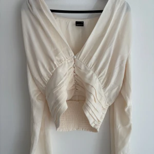 Krämvit omlott blus med v-ringning - Superfin krämvit blus från gina tricot med djup v-ringning, omlott-effekt och smockad midja. Isatinliknande material med vackra puffärmar och draperad effekt som framhäver midjan på ett superfint sätt. Använd en gång i nyskick!😍