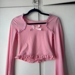 Rosa långärmad topp med volang - Supersöt rosa långärmad topp med spetsdetaljer runt halsen, liten rosett framtill och volangkant nedtill, från SHEIN. Perfekt för dig som gillar en gullig stil. Croppad modell som passar till både jeans och kjol. Hör av dig om du vill ha fler bilder eller har några frågor! 