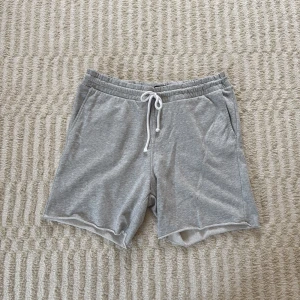 Grå mjuka shorts från H&M - Gråa shorts från i mjuk bomull med elastisk midja och vit snörning. Regular fit med fickor på sidorna och en bakficka. Det finns en liten fläck vid ena låret (se sista bild)!