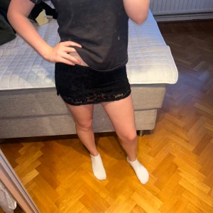 Svart minikjol i spets - Supersnygg svart minikjol med spetsdetaljer och tajt passform. Den har även korta svarta undershorts.