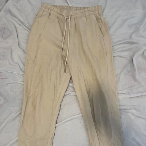 Beiga linnebyxor med snörning - Snygga beiga linnebyxor med elastisk midja och snörning framtill. Byxorna har raka ben och sidofickor, samt en bakficka. Perfekta för en chill och avslappnad stil under varmare dagar.