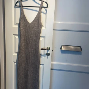 Ribbad beige långklänning H&M - Ribbad beige långklänning från H&M med v-ringning och ärmlös design. Klänningen har en slim passform och en liten slits bak för extra rörelsefrihet. Perfekt för dig som gillar en enkel men stilren look.