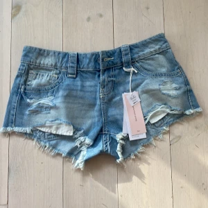Lågmidjade jeansshorts Gina Tricot XS - Snygga lågmidjade jeansshorts från Gina Tricot i ljusblå denim. Modellen är extra kort med slitna detaljer, fransig kant och klassiska fickor fram och bak. .
