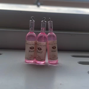 Örhängen med rosa vinflaskor -   ALLA = 32 + frakt.   2 vinflaskor= 26 .   1 vinflaska = 12kr.    HÖR AV DIG OM DU VILL VETA MER OM PRISER!  unika örhängen formade som små vinflaskor med rosa vätska och etikett med texten 'Cabernet Sauvignon'. Flaskorna har silverfärgade detaljer upptill och ögla för upphängning. Perfekt accessoar för dig som vill sticka ut med en lekfull och trendig stil. 
