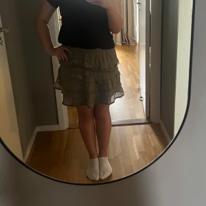 Beige volangkjol från Neo Noir - Supersöt beige kortkjol från Neo Noir med flera volanglager och smock i midjan. Kjolen har en luftig känsla och passar perfekt till en avslappnad stil. Den är lätt att matcha med både t-shirt och stickad tröja.