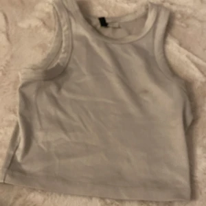 Vit ribbad linnetopp från H&M Divided XS - Säljer en enkel och stilren vit ribbad linnetopp från H&M Divided i storlek XS. Toppen är ärmlös med klassisk rund halsringning och croppad passform. Perfekt till jeans eller kjol för en clean look. Men en fläck. 